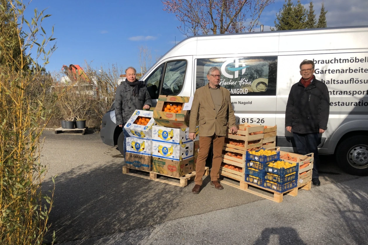 Drei Personen stehen vor einem Transporter mit dem Logo der Erlacher H&ouml;he. Vor ihnen stehen mehrere Kisten mit Orangen und Mandarinen.