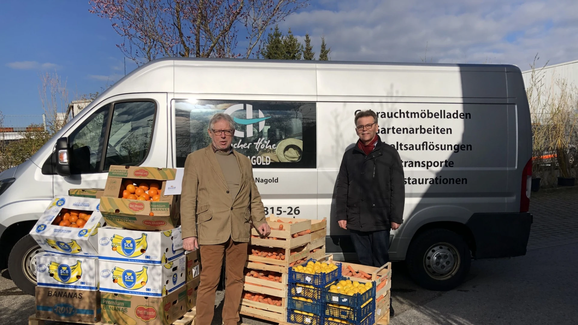 Zwei Personen stehen vor einem Transporter mit dem Logo der Erlacher H&ouml;he. Vor ihnen stehen mehrere Kisten mit Orangen und Mandarinen.