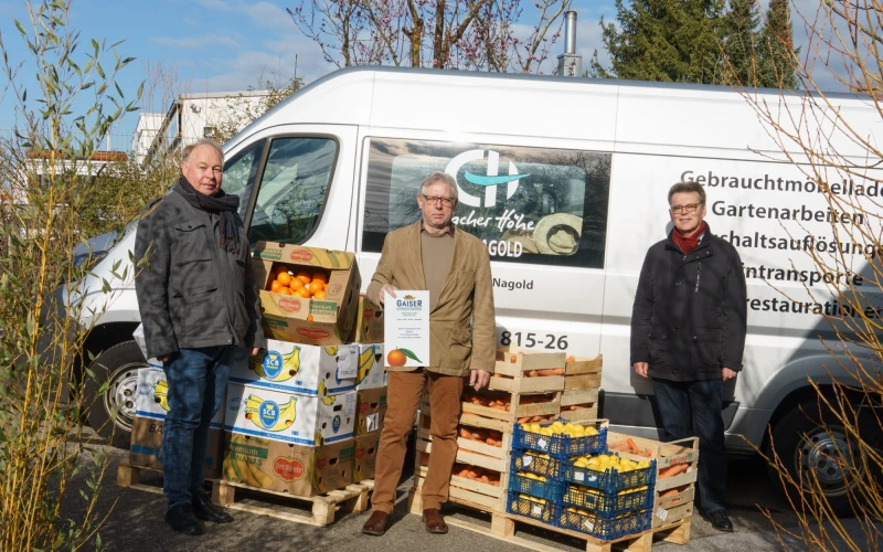 Drei Personen stehen vor einem Transporter mit dem Logo der Erlacher H&ouml;he. Vor ihnen stehen mehrere Kisten mit Orangen und Mandarinen.