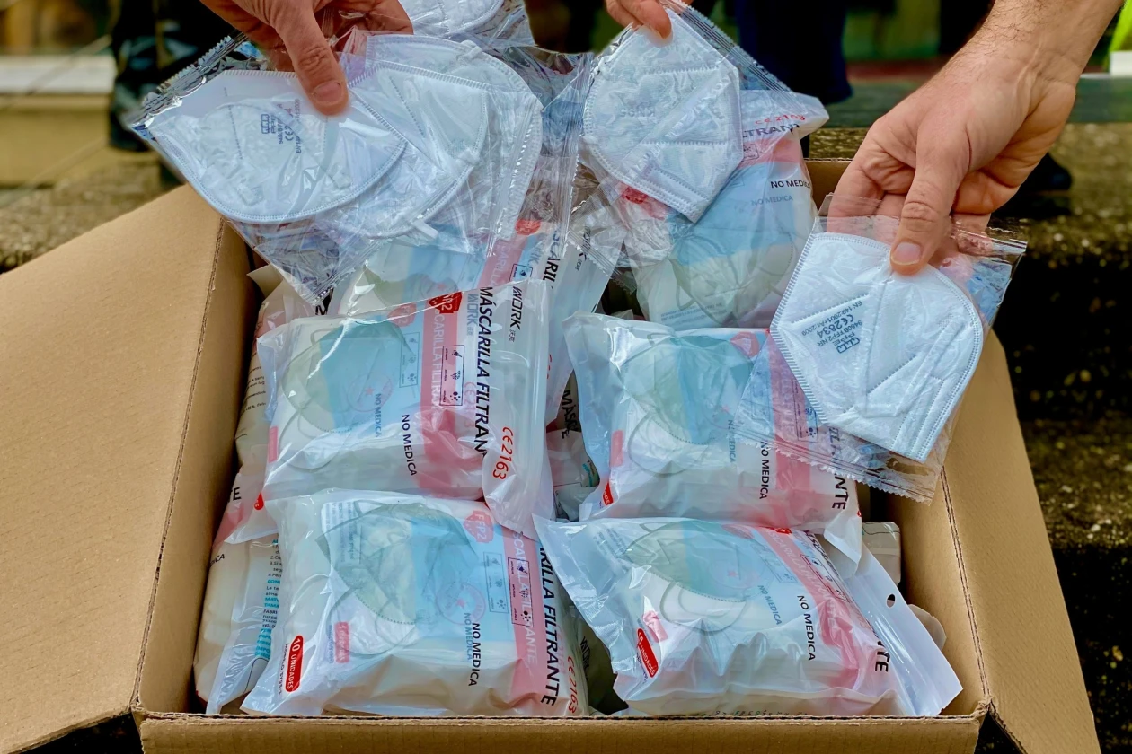 H&auml;nde halten mehrere einzeln verpackte wei&szlig;e FFP3-Masken aus einem Karton. Die Masken sind in durchsichtigen Plastikt&uuml;ten mit roten Etiketten verpackt.