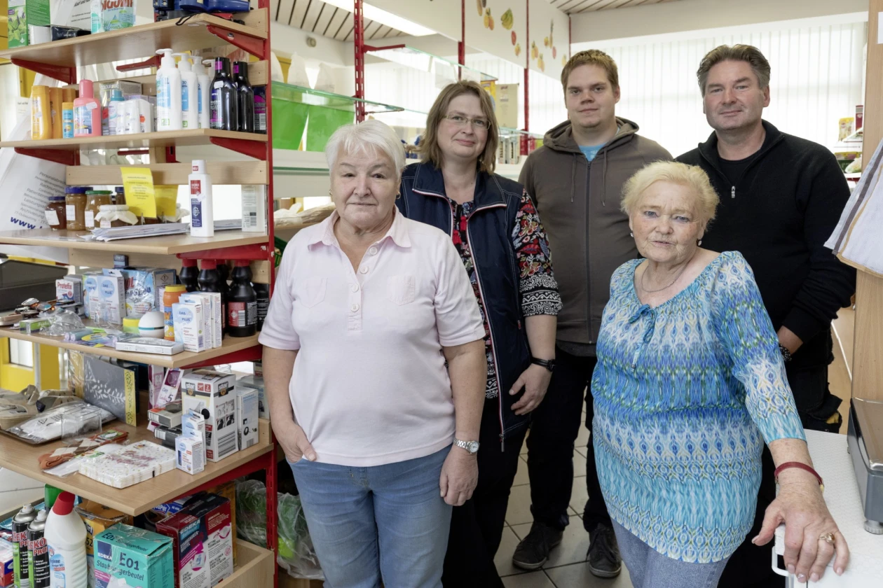 F&uuml;nf Personen stehen in einem Raum mit Regalen voller Haushaltswaren. Zwei Frauen stehen vorne und drei weitere Personen dahinter, sie blicken alle in die Kamera.