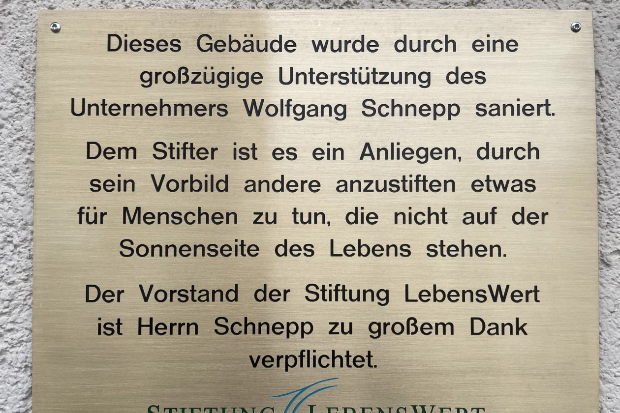 Messingfarbene Gedenktafel der Stiftung LebensWert, die Wolfgang Schnepp f&uuml;r seine gro&szlig;z&uuml;gige Unterst&uuml;tzung und sein soziales Engagement w&uuml;rdigt, angebracht auf einer wei&szlig;en Wand.