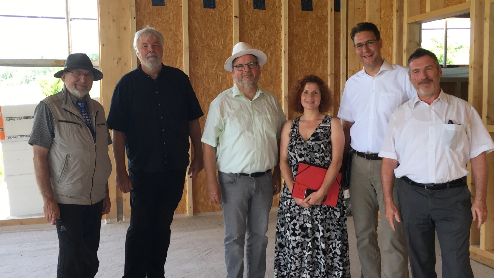 Sechs Menschen in einem Neubau vor Holzst&auml;nderw&auml;nden. Sie blicken in die Kamera und l&auml;cheln.