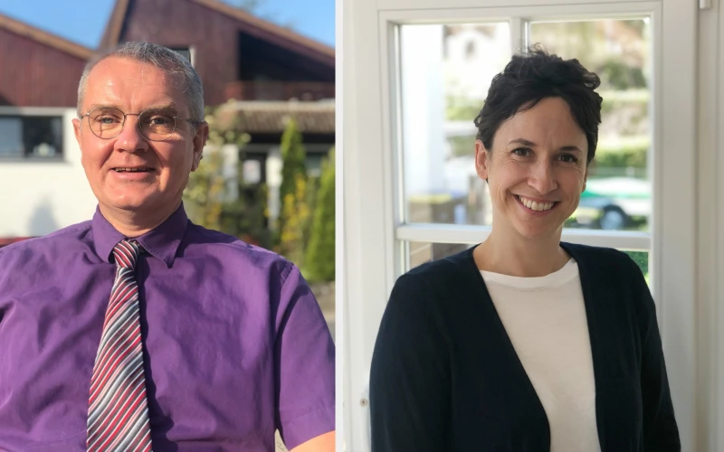 Links im Bild ist ein Mann zu sehen, der eine Brille, ein lila Hemd und eine gestreifte Krawatte tr&auml;gt. Er steht vor einem Haus, das von B&auml;umen umgeben ist. Rechts im Bild befindet sich eine Frau, die eine schwarze Strickjacke &uuml;ber einem wei&szlig;en Oberteil tr&auml;gt. Sie steht vor einem Fenster. Beide l&auml;cheln in die Kamera.