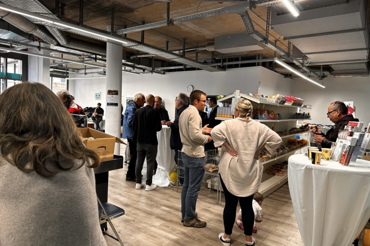 Besuchergruppe in einem modernen Ladenraum im Industrielook mit offener Decke, Regalen und einer Theke. Mehrere Personen stehen und unterhalten sich in verschiedenen Bereichen des Raumes.