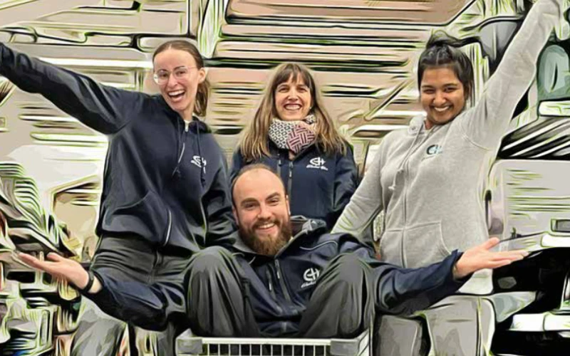 Vier Personen strahlen in die Kamera. Sie strecken die Arme zu einer herzlichen Begr&uuml;&szlig;ung aus und sitzen bzw. stehen nebeneinander vor einem abstrakten, skizzierten Hintergrund.