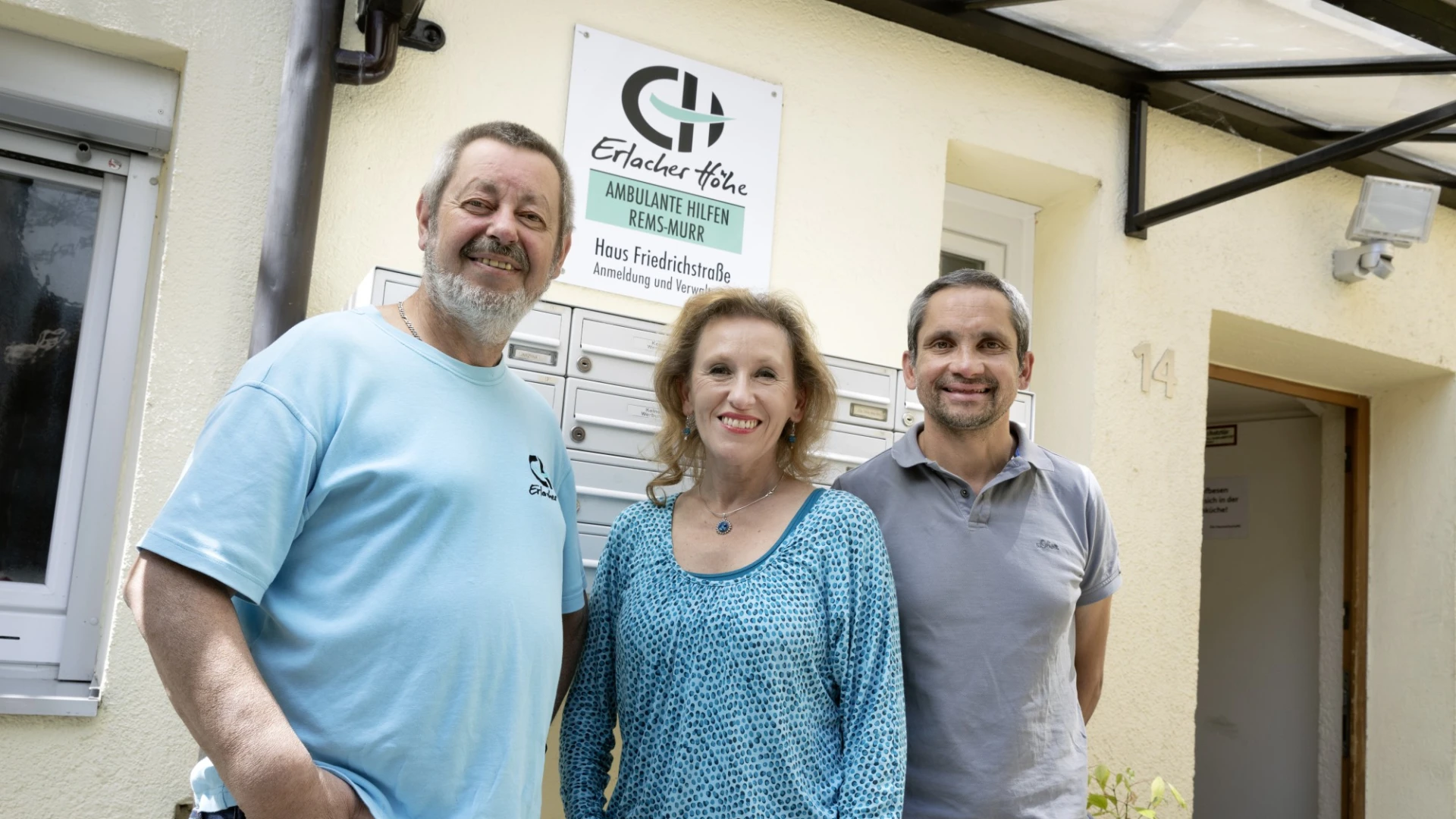 Zwei M&auml;nner und eine Frau stehen vor einem Geb&auml;ude mit der Beschilderung Erlacher H&ouml;he "Ambulante Hilfen Rems-Murr".
