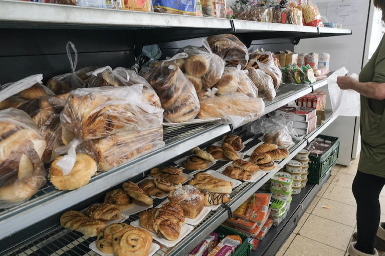 Regale mit Geb&auml;ckst&uuml;cke in verschiedenen Formen und Gr&ouml;&szlig;en, in Plastikt&uuml;ten verpackt und offen pr&auml;sentiert. Weitere Lebensmittel sind zu sehen. Eine Frau steht vor dem Regal und schaut sich die Backwaren an.