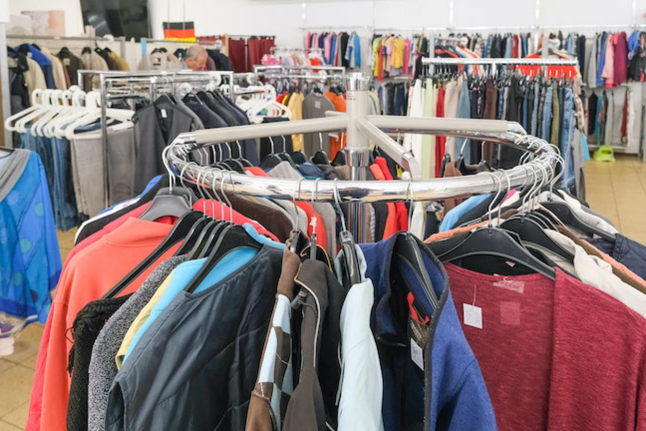 Runder Kleiderst&auml;nder mit verschiedenfarbigen Kleidungsst&uuml;cken wie Pullovern, Jacken und Shirts. Im Hintergrund weitere Kleidungsst&uuml;cke an Kleiderstangen.