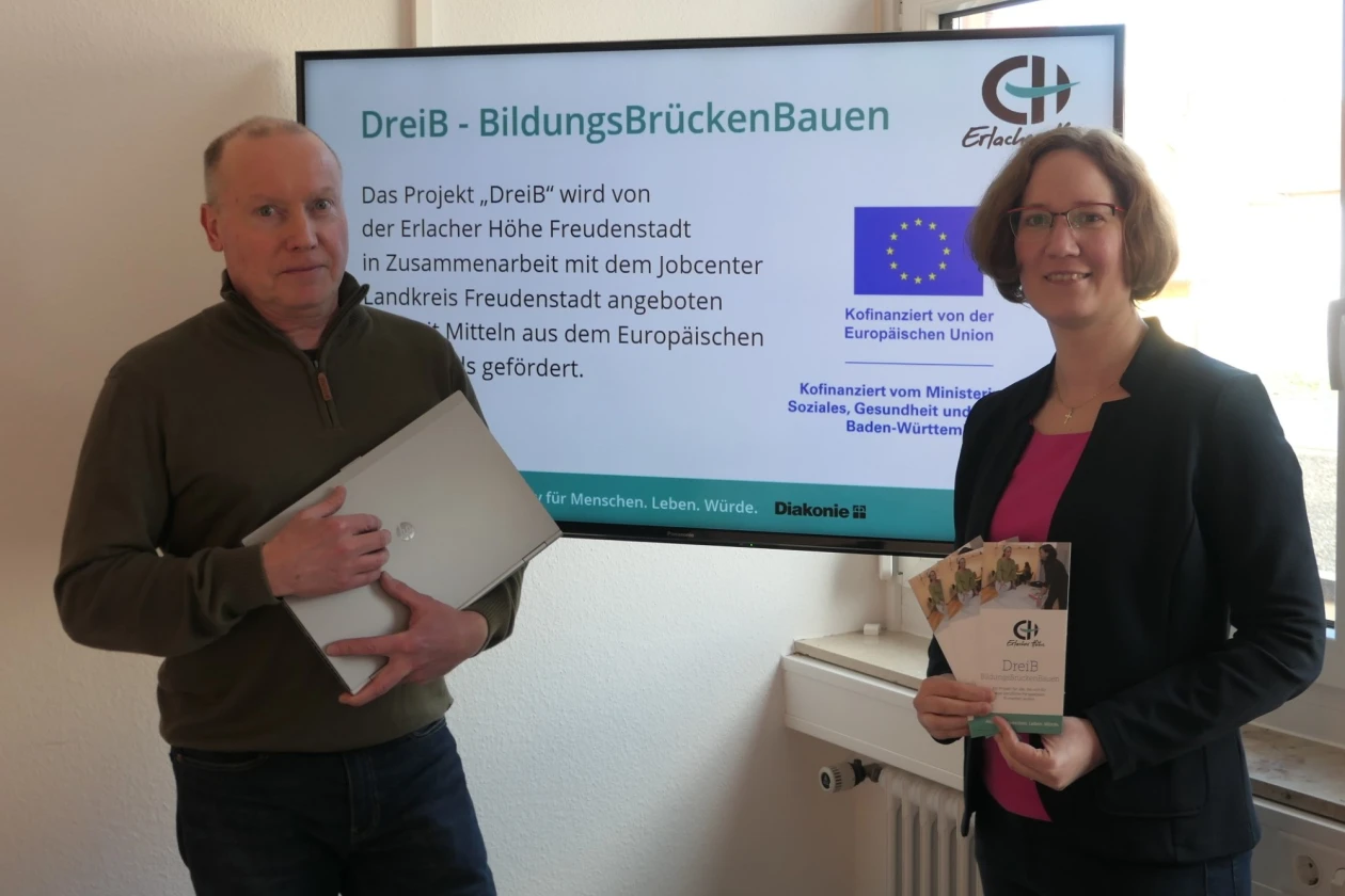 Zwei Personen pr&auml;sentieren das Projekt "DreIB - BildungsBr&uuml;ckenBauen" vor einer Informationstafel