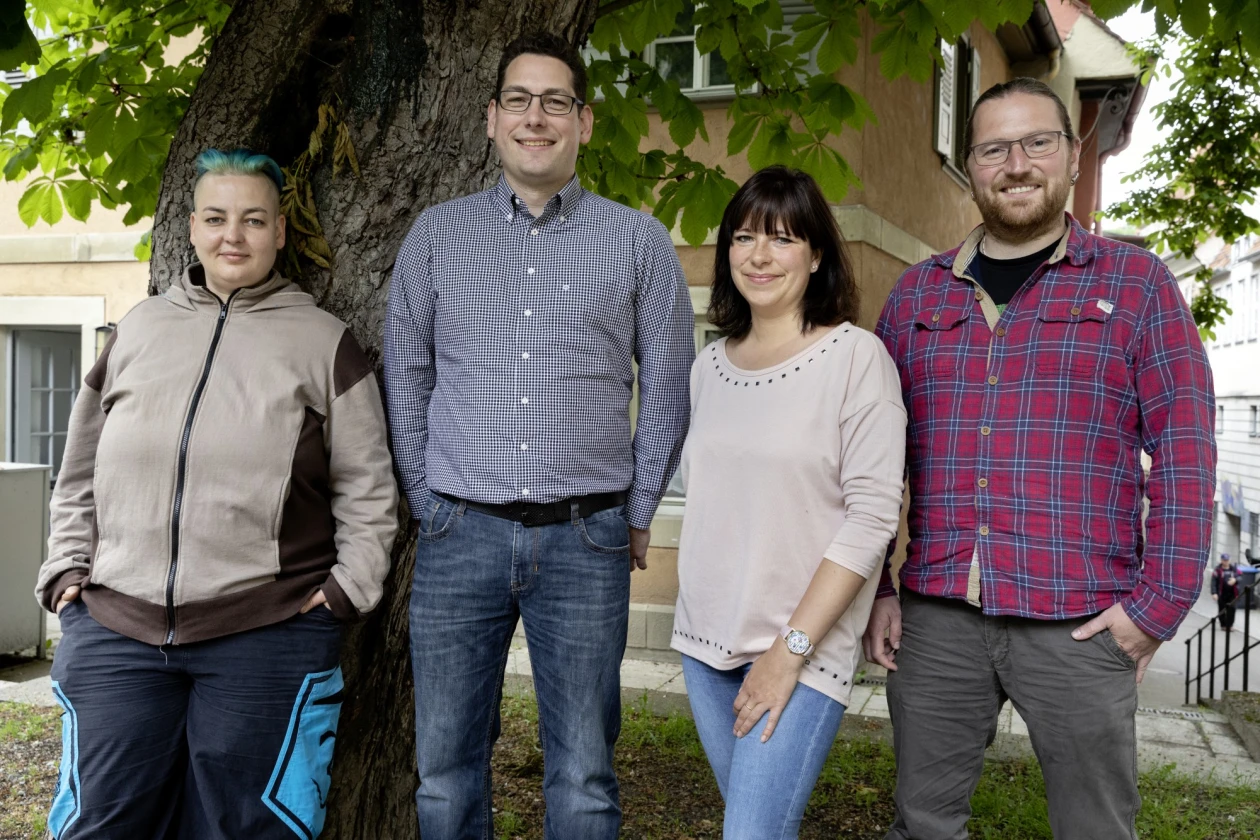 Zwei Frauen und zwei M&auml;nner stehen vor einem gro&szlig;en Baum und l&auml;cheln freundlich in die Kamera. Leger gekleidet vermitteln sie einen entspannten, teamorientierten Eindruck.