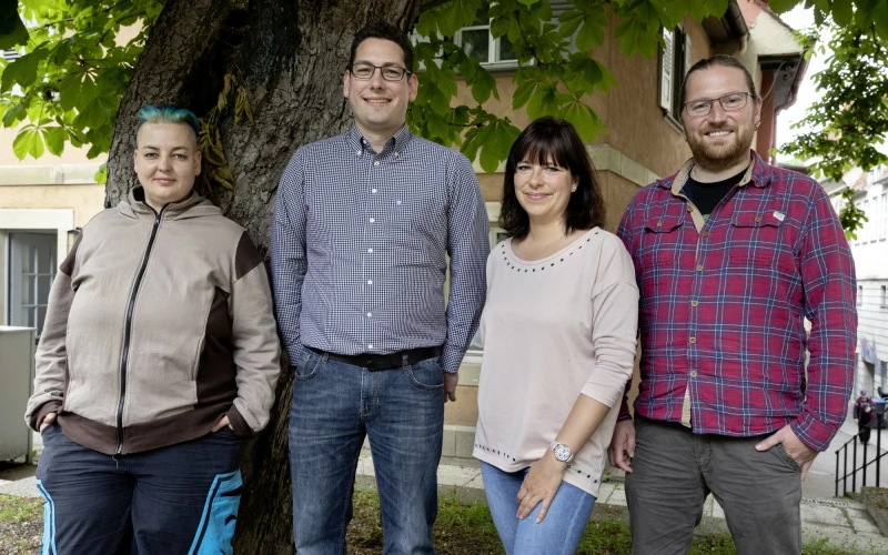 Zwei Frauen und zwei M&auml;nner stehen vor einem gro&szlig;en Baum und l&auml;cheln freundlich in die Kamera. Leger gekleidet vermitteln sie einen entspannten, teamorientierten Eindruck.