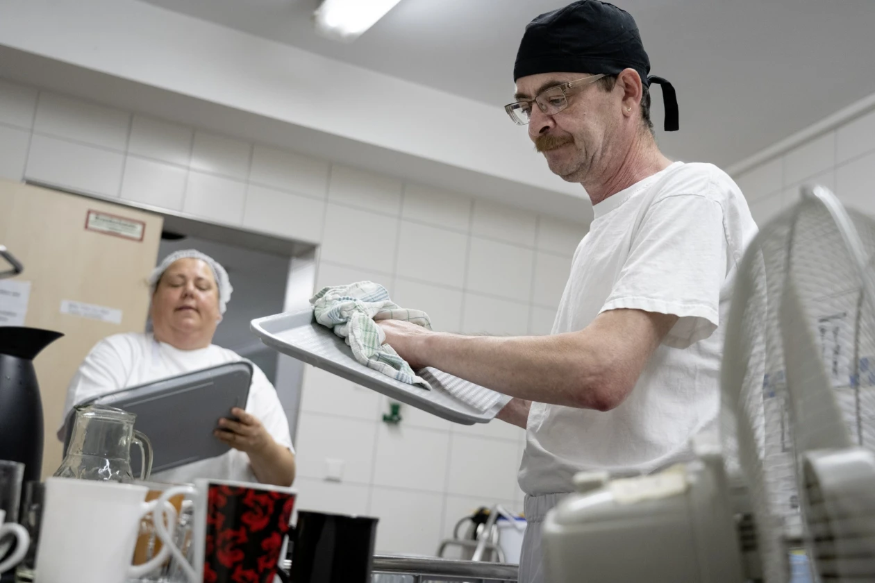 Zwei Personen in wei&szlig;er K&uuml;chen-Arbeitskleidung und Kopfhauben in einer K&uuml;che arbeitend. Beide halten Tabletts in der Hand, die sie abtrochken.