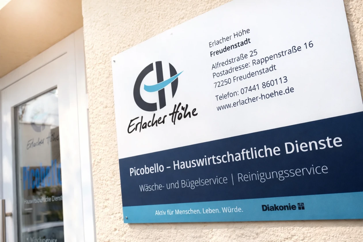 Man sieht ein Eingangsschild von unserer Hauswirtschaft Namens Picobello mit weiteren Infos wie Stra&szlig;e, Telefonnummer, Homepage. Im Hintergrund sieht man die Eingangst&uuml;re