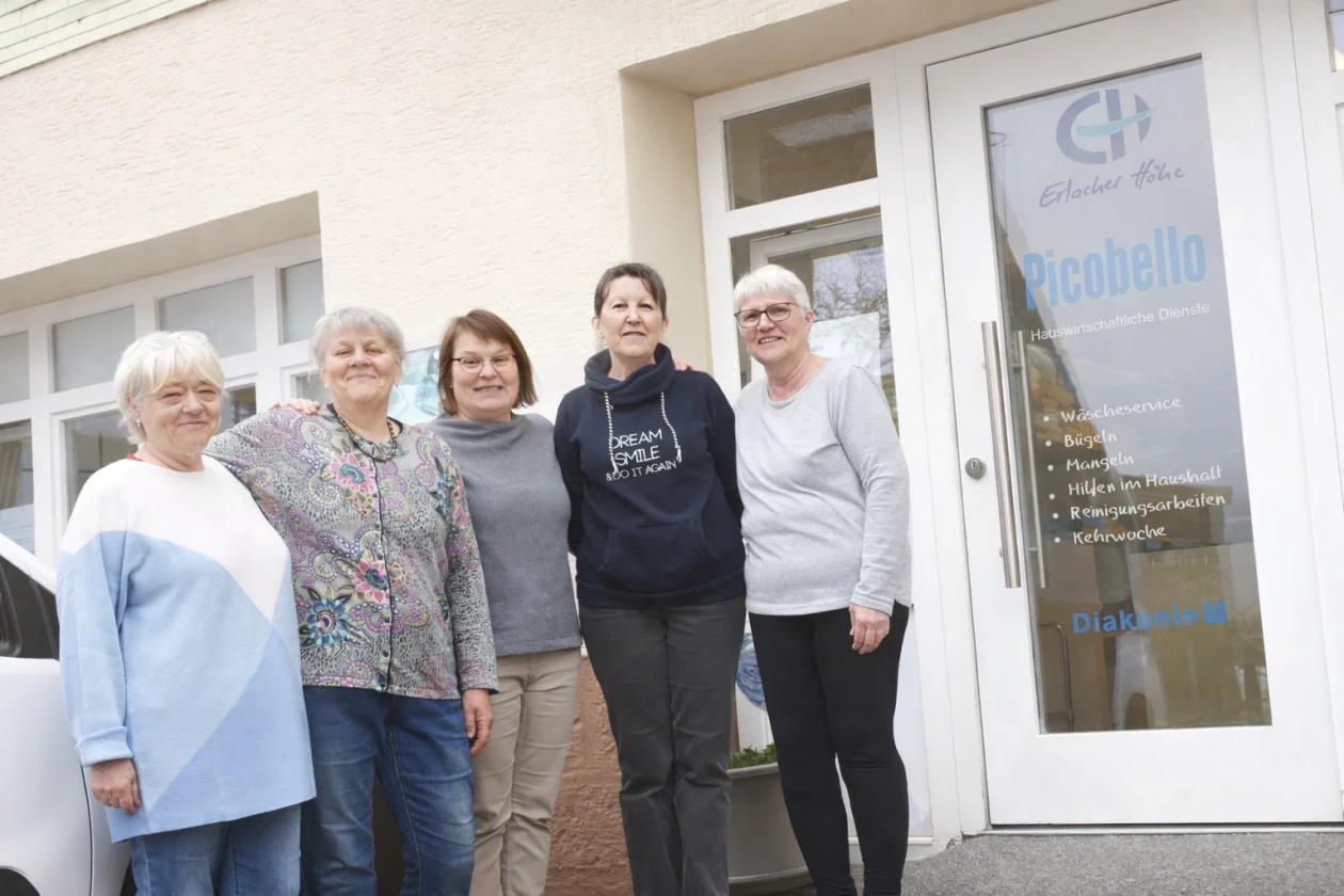 Die Damen unserers W&auml;scheservice lachen gemeinsam auf einem Gruppenfoto vor der Eingangst&uuml;r Picobello.