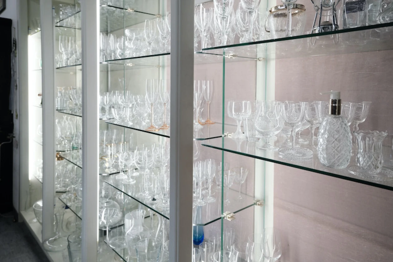 Transparente Glasvitrine mit mehreren Regalen, gef&uuml;llt mit verschiedenen Kristallgl&auml;sern und Kelchen in unterschiedlichen Formen und Gr&ouml;&szlig;en.