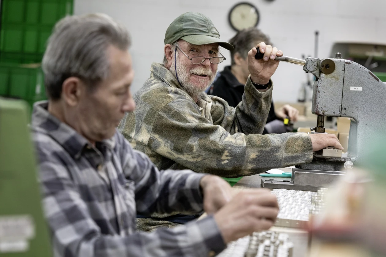 Zwei &auml;ltere M&auml;nner arbeiten konzentriert an Maschinen in einer Werkstatt. Beide tragen karierte Hemden und konzentrieren sich auf ihre Arbeit.