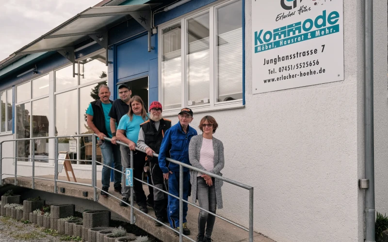 Sechs Personen stehen auf der Rampe vor dem Geb&auml;ude der Kommode Horb der Erlacher H&ouml;he. Hinter ihnen befinden sich gro&szlig;e Fenster und eine auff&auml;llige blaue Eingangst&uuml;r.