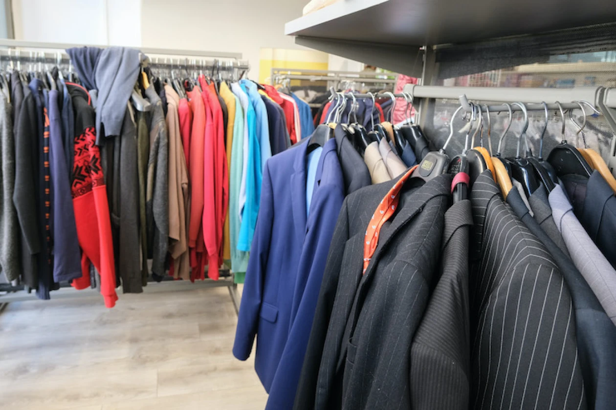 Verschiedene Kleidungsst&uuml;cke und M&auml;ntel in unterschiedlichen Farben h&auml;ngen auf Kleiderb&uuml;geln an einer Kleiderstange.