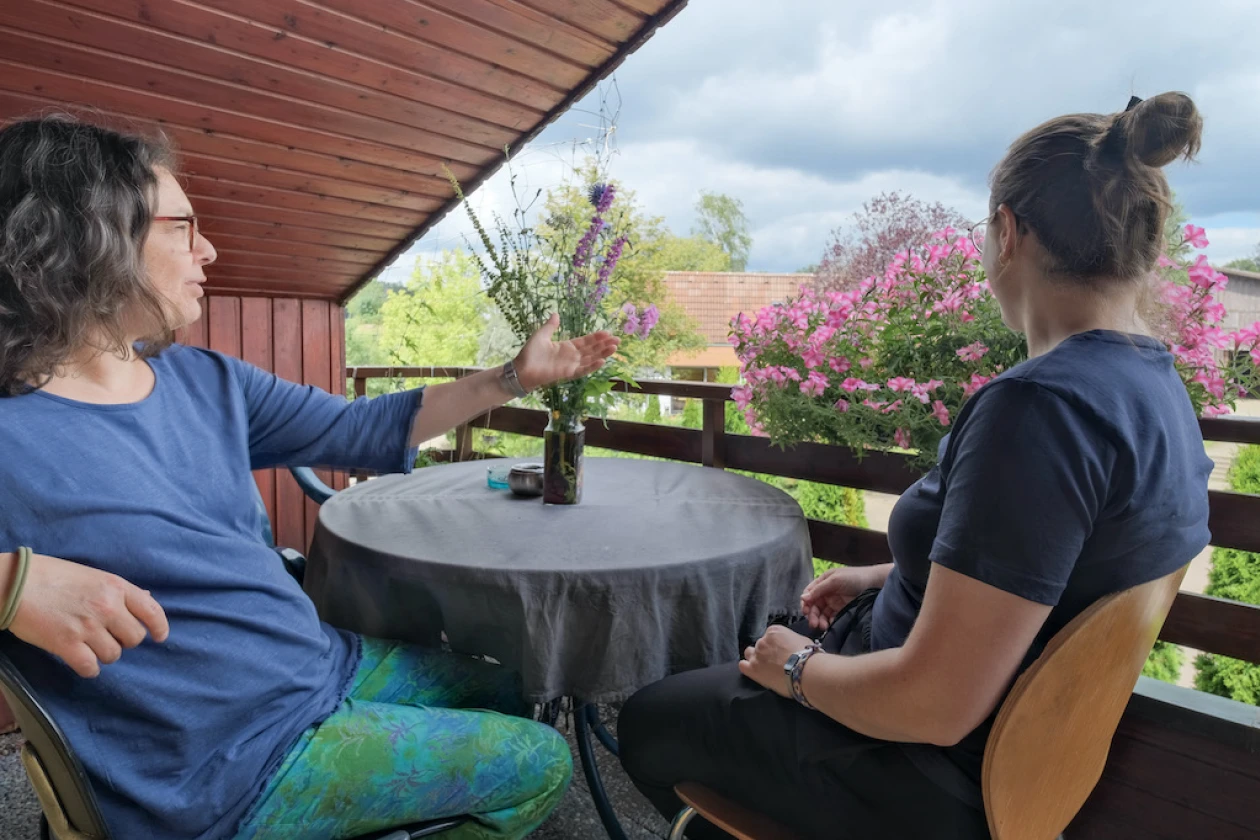 Zwei Frauen sitzen auf einem Balkon an einem runden Tisch und genie&szlig;en die Aussicht.
