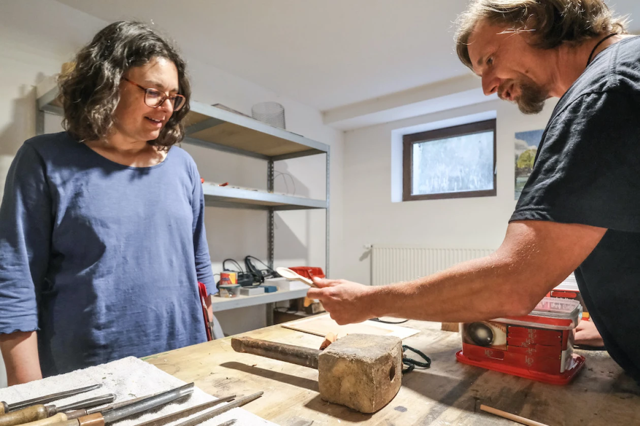 In einer Kreativwerkstatt stehen eine Frau und ein Mann an einem Arbeitstisch mit Werkzeugen und Kreativmaterialien.