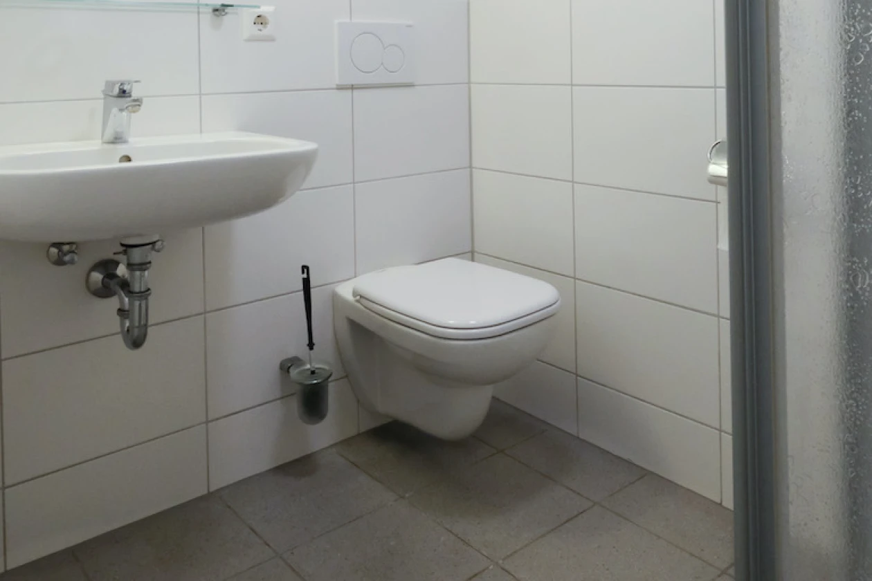 Zu sehen ist eine Toilette, ein Waschbecken, eine Dusche und ein kleiner Spiegel &uuml;ber dem Waschbecken.