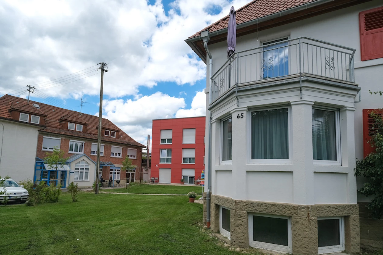 Blick auf ein Geb&auml;udearrangement unterschiedlicher Epochen. Im Vordergrund Teil einer Villa mit turmf&ouml;rmigem Balkon, dahinter ein quaderf&ouml;rmiger, roter Hauskomplex und daneben ein gr&ouml;&szlig;eres Geb&auml;ude aus Klinkerstein mit drei Gauben auf dem Dach.