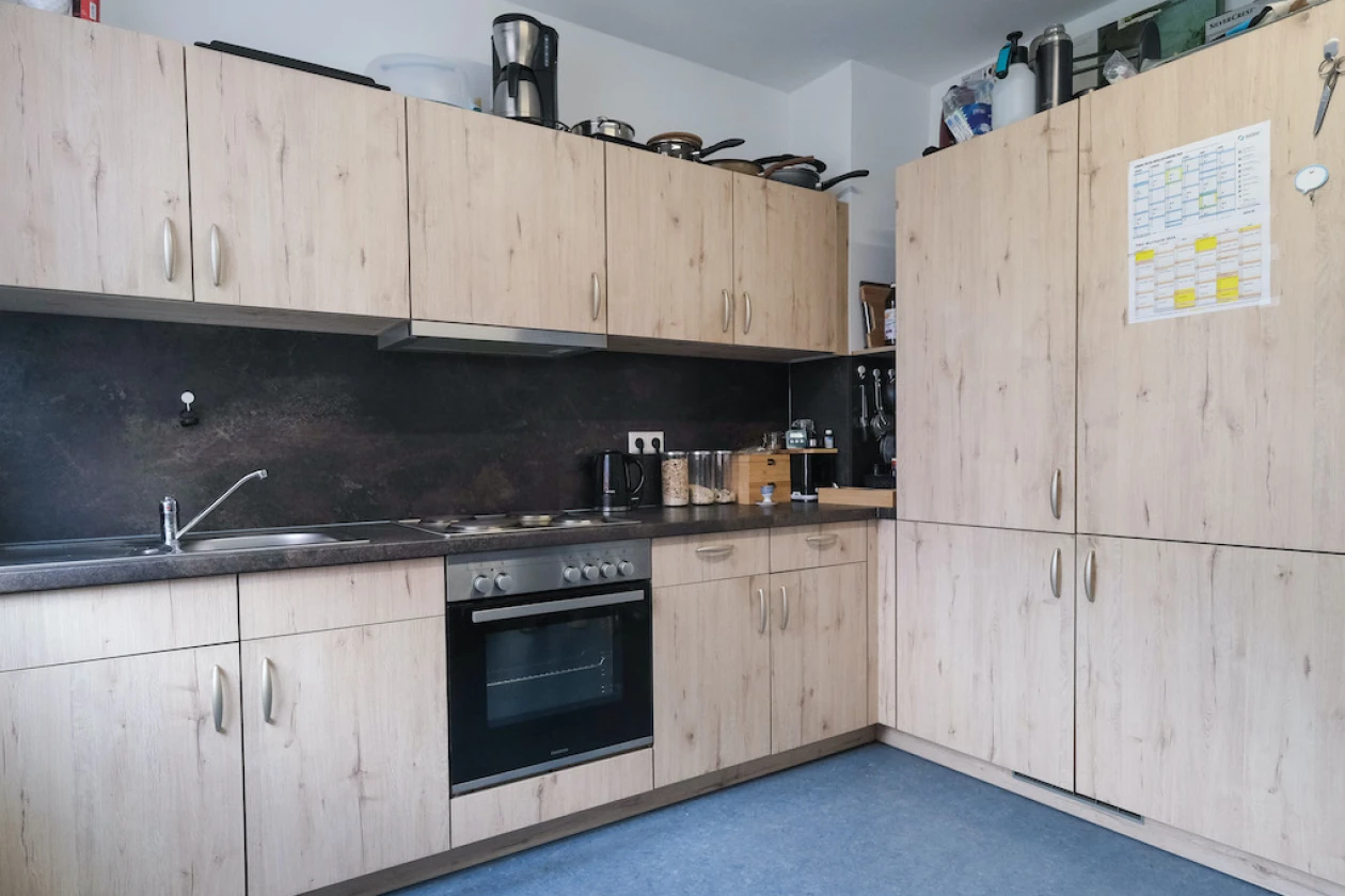 Moderne L-f&ouml;rmige K&uuml;che mit hellen Holzfronten, dunkler Arbeitsplatte und R&uuml;ckwand, ausgestattet mit Einbauger&auml;ten wie Herd und Dunstabzugshaube.