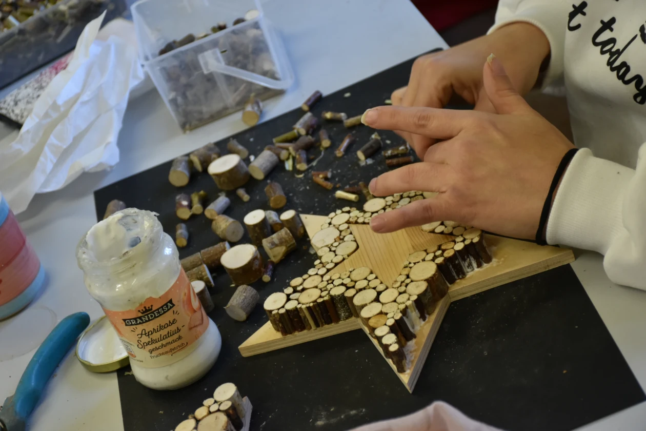 Eine Mitarbeiterin beklebt einen Holzsstern mit kleinen Holz&auml;sten. Im Hintergrund sieht man ganz viele Holz&auml;ste und Holzleim.