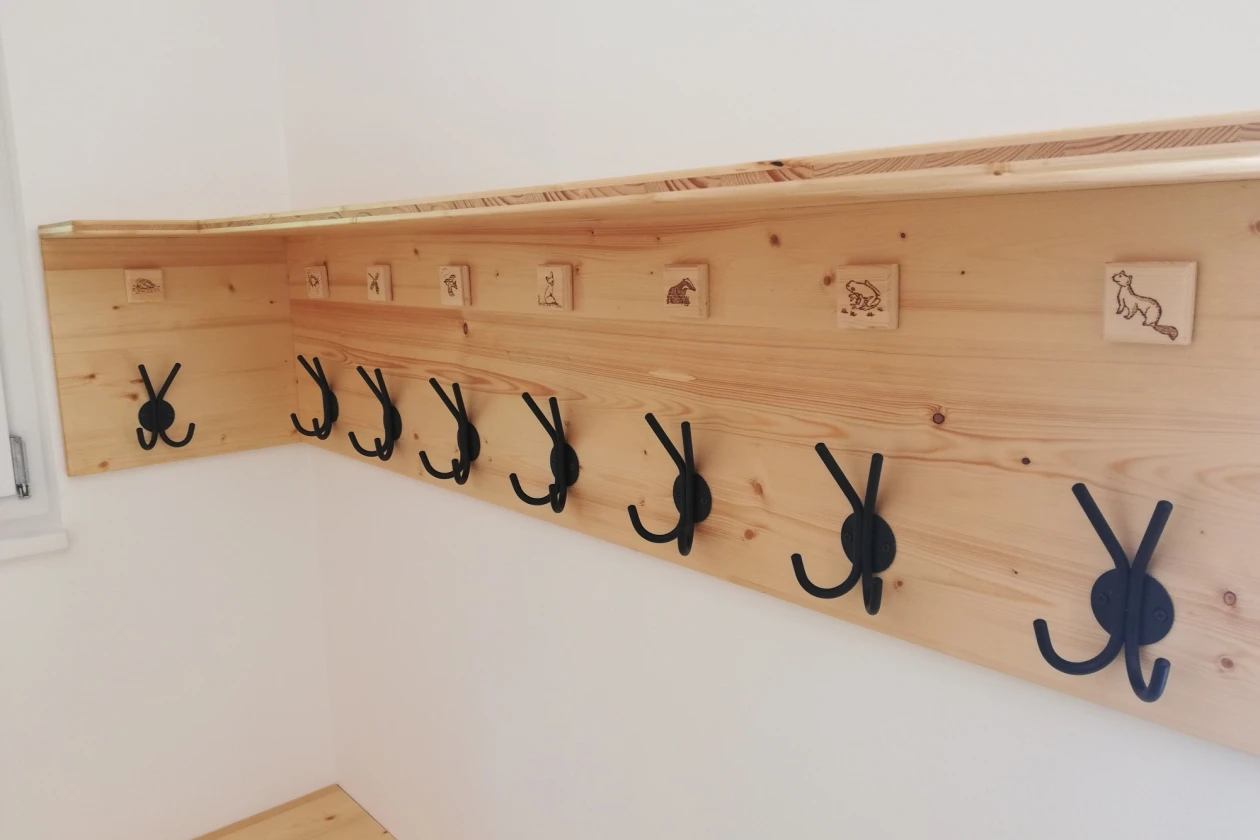 Eine Holzgarderobe h&auml;ngt an der Wand. &Uuml;ber den Kleiderhaken sind Schildchen mit Tieren angebracht.