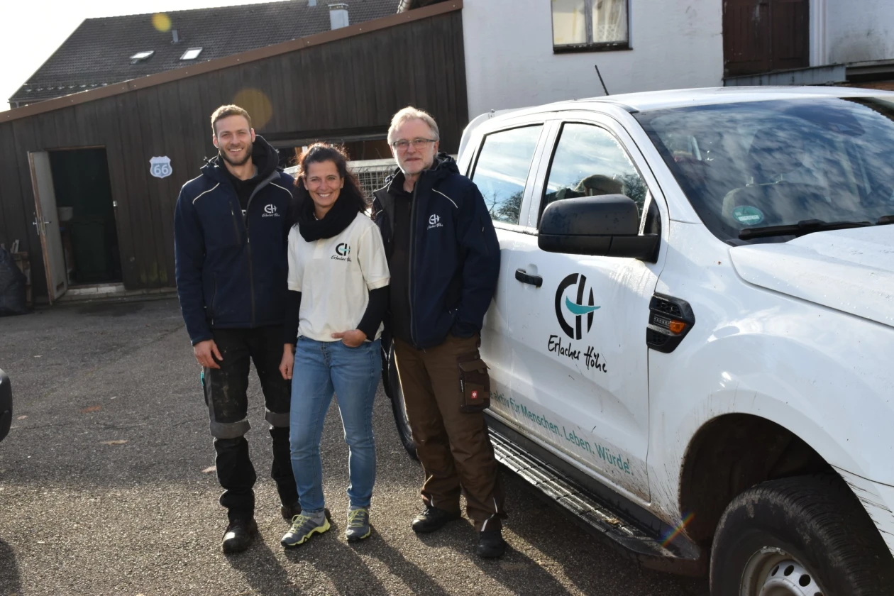Drei Personen stehen vor einem wei&szlig;en Transporter mit dem Logo der Erlacher H&ouml;he in einem Innenhofbereich.