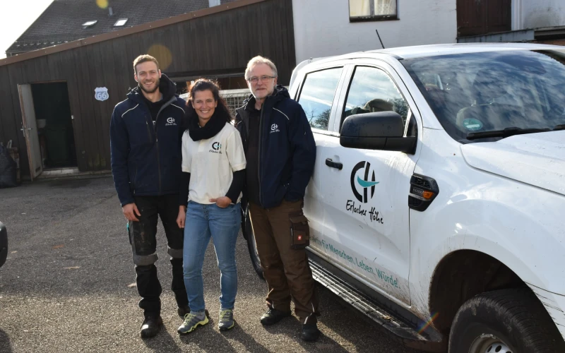 Drei Personen stehen vor einem wei&szlig;en Transporter mit dem Logo der Erlacher H&ouml;he in einem Innenhofbereich.