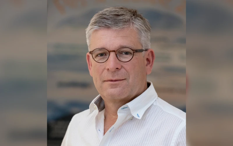 Ein Mann mit grauen Haaren und runder Brille, gekleidet in ein wei&szlig;es gestreiftes Hemd, blickt frontal in die Kamera vor einem unscharfen Hintergrund.